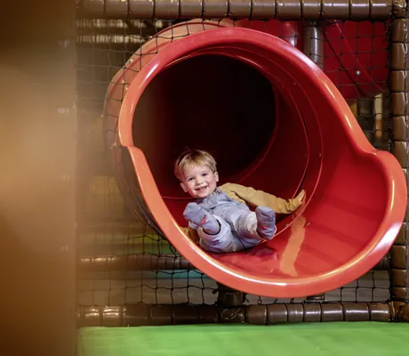 Kind rutscht durch eine rote Röhrenrutsche in einem Indoor-Spielbereich des Familotel Elldus Resort