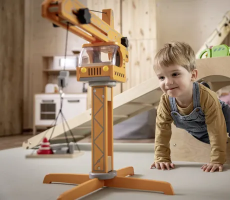 Kind spielt in einem Spielzimmer des Familotel Elldus Resort mit Holzspielzeug und Kinderküche im Hintergrund