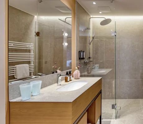 Elegantes, schlichtes Badezimmer im Falkensteiner Family Hotel Montafon mit Regendusche, Waschbecken und modernen Armaturen