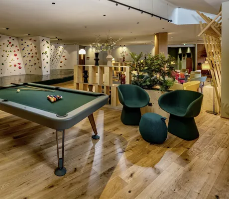 Billardtisch und Indoor-Kletterwand in der modernen Lobby des Falkensteiner Family Hotels Montafon mit gemütlichen Sitzbereichen