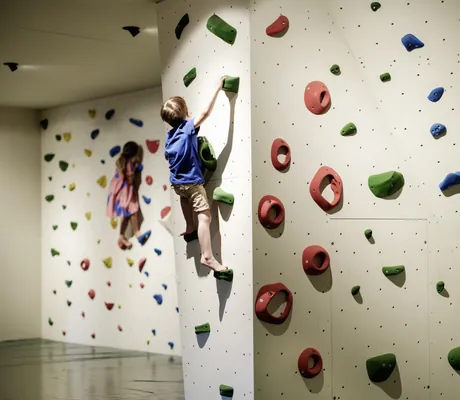 Kinder erklimmen eine Indoor-Kletterwand im Falkensteiner Family Hotel Montafon, farbenfrohe Klettergriffe im Fokus