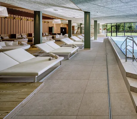 Moderner Indoorpool im Falkensteiner Family Hotel Montafon mit Liegen und Panoramafenstern zum Garten