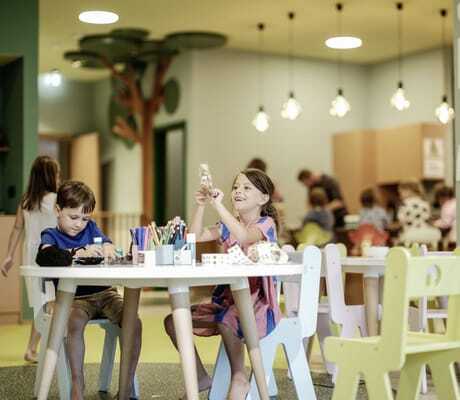 Kinder basteln und spielen im Kidsclub des Falkensteiner Family Hotels Montafon, Kinderbilder an der Wand im Hintergrund