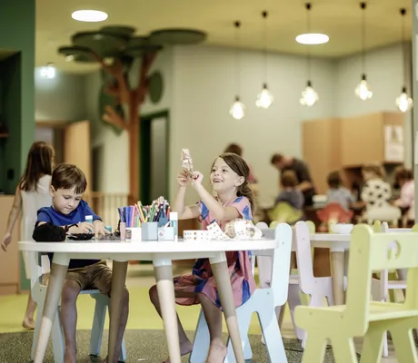 Kinder basteln und spielen im Kidsclub des Falkensteiner Family Hotels Montafon, Kinderbilder an der Wand im Hintergrund