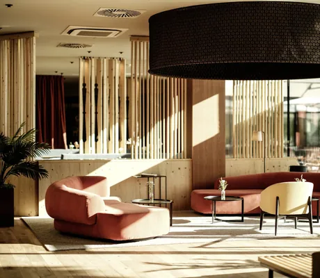 Gemütliche Lobby im Falkensteiner Family Hotel Montafon mit modernen roten und gelben Sitzmöbeln und warmem Lichteinfall