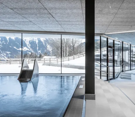 Poolbereich im Falkensteiner Family Hotel Montafon mit Kinderbecken, Wasserrutsche und Blick auf die verschneite Berglandschaft