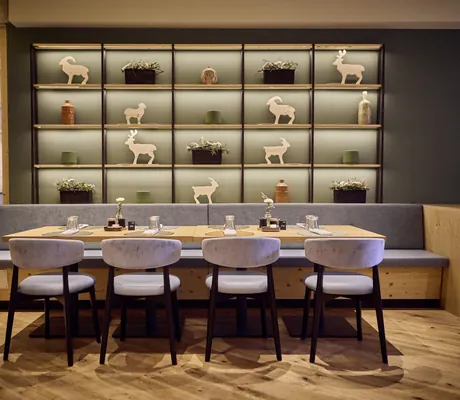 Stilvolles Restaurant im Falkensteiner Family Hotel Montafon mit dekorativem Wandregal, gedecktem Tisch und grauen Sitzmöbeln