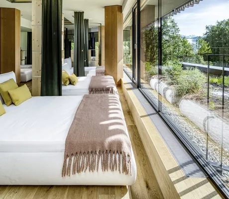 Wellnessbereich im Falkensteiner Family Hotel Montafon mit bequemen Liegen, grün-gelben Kissen und Panoramaglasfront mit Blick in die Natur