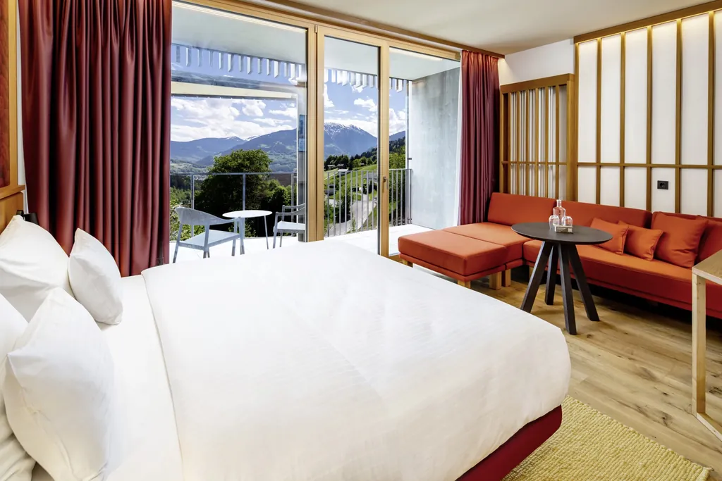 Zimmer mit Doppelbett und rotem Sofa im Falkensteiner Family Hotel Montafon, Balkon mit Sitzgruppe und Bergpanorama