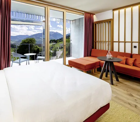 Zimmer mit Doppelbett und rotem Sofa im Falkensteiner Family Hotel Montafon, Balkon mit Sitzgruppe und Bergpanorama
