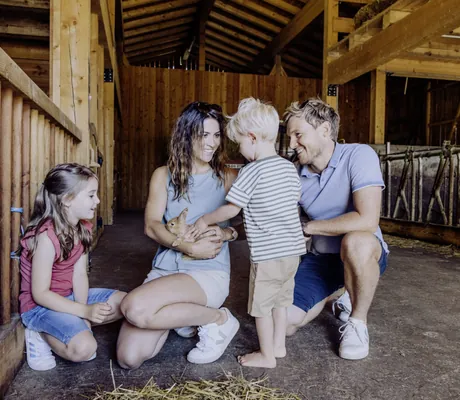 Familie in Scheune des Bauernhofs im Naturresort PURADIES mit Kaninchen im Arm im Naturresort PURADIES