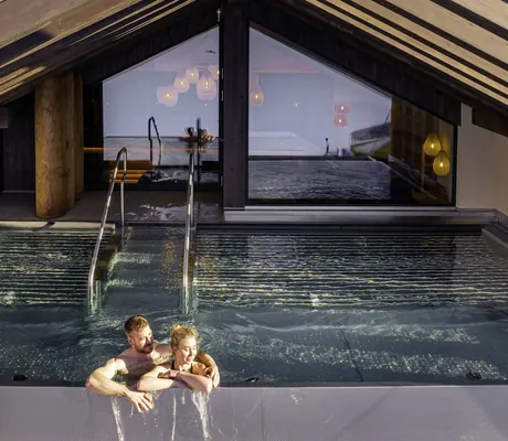 Infinity-Whirlpool im Familotel Zauchenseehof unter einem Holzdach, zwei Personen im Wasser am Beckenrand