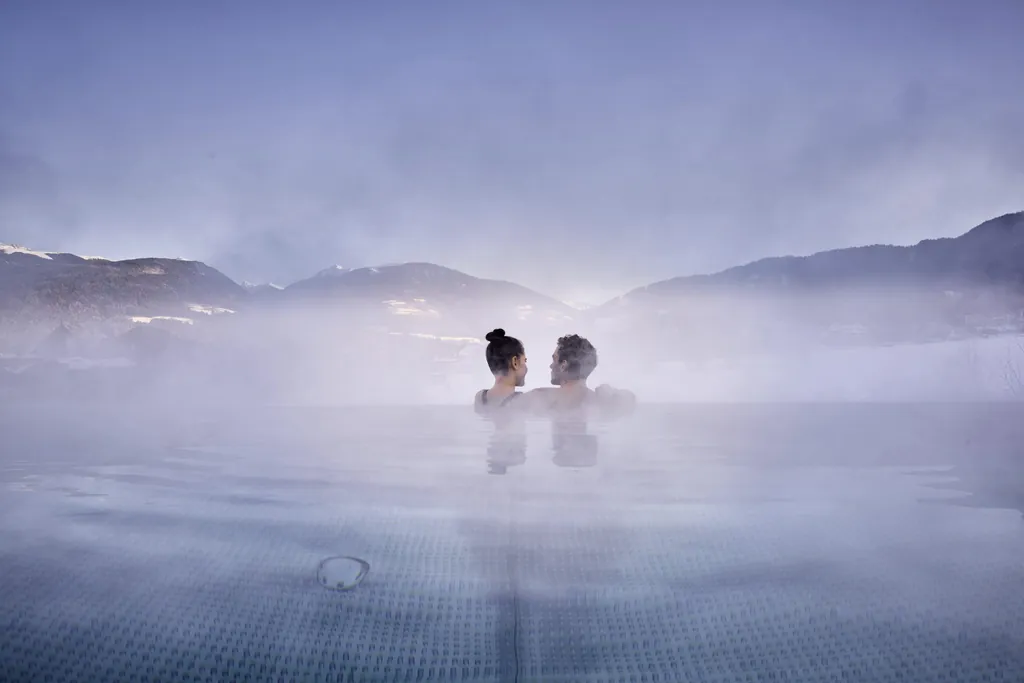 Pärchen im Sky-Infinitypool mit Blick auf Berglandschaft, umgeben von Wärmewolken