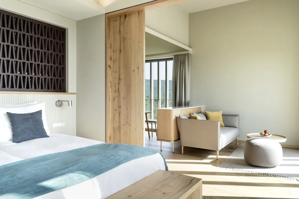 Zimmer im WALD.WEIT mit türkisem Bettüberwurf und Sitzecke mit grauem Sofa