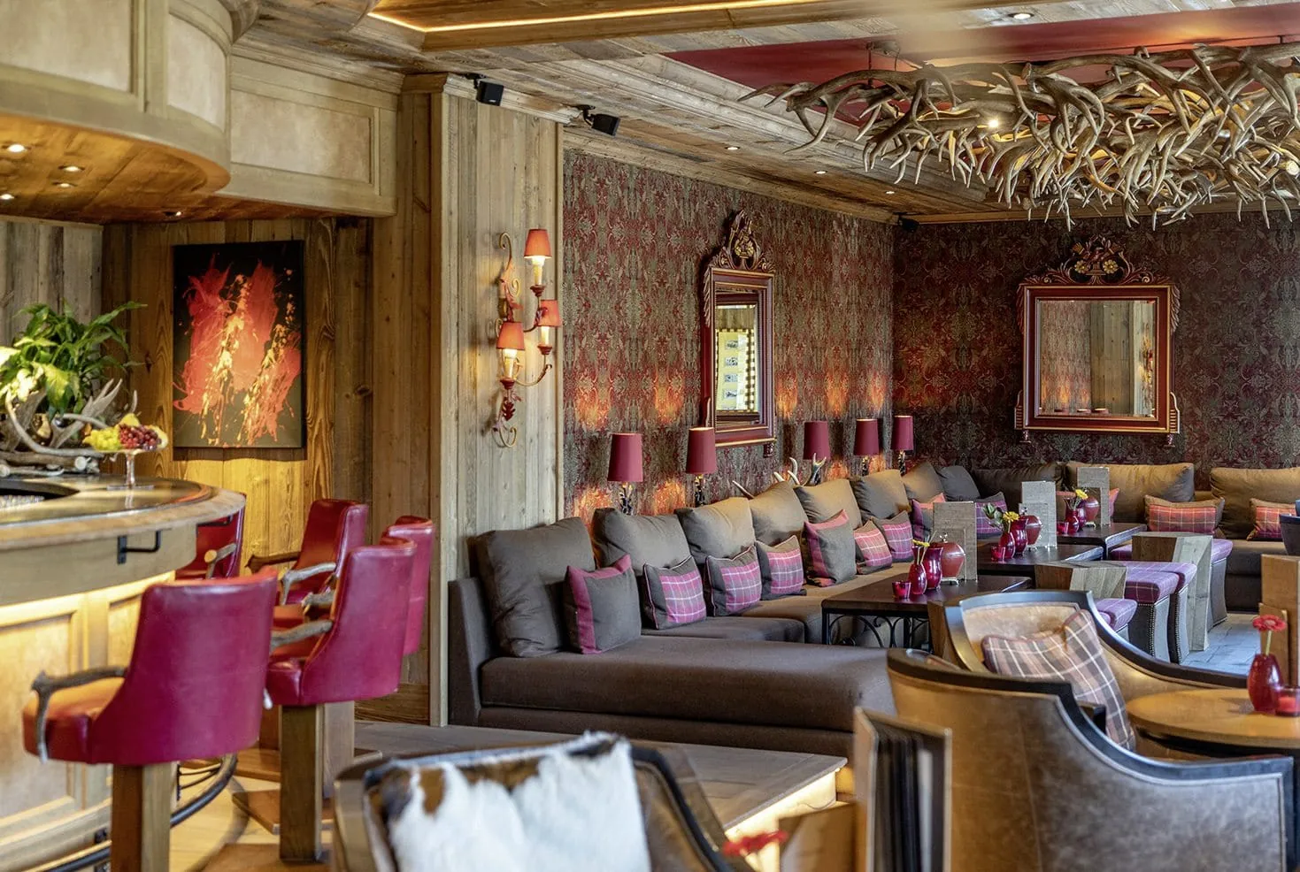 Blick von der Bar im Alpin Resort Sacher Seefeld &ndash; Tirol mit roten Ledersesseln auf Loungeecke mit Geweihen an der Decke