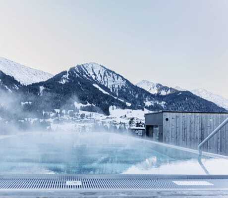 Sky-Infinitypool im Morgengrauen vor schneebedeckten Berghängen des Hotels Sonnenburg.