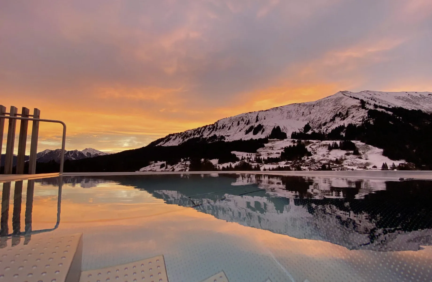 Blick auf den schneeüberzogenen Berghang bei Sonnenaufgang vom Infinitypool des Hotels Sonnenburg.