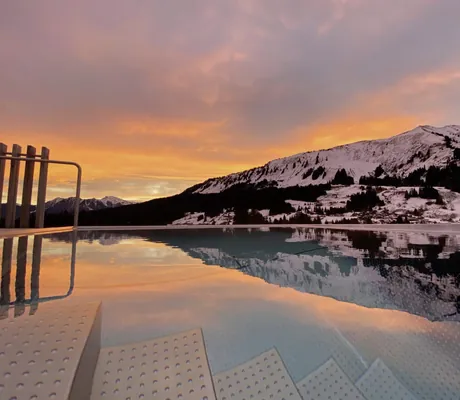 Blick auf den schneeüberzogenen Berghang bei Sonnenaufgang vom Infinitypool des Hotels Sonnenburg.