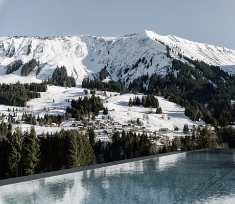 Blick vom Sky-Infinitypool des Aktivhotels Sonnenburg mit schneebedeckten Berghängen und Bäumen.