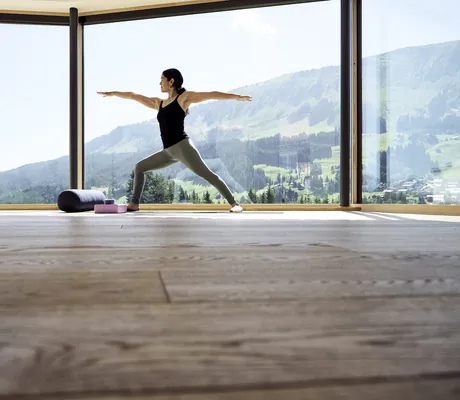 Eine Frau in der Yogaposition des Sonnenkriegers im Fitnessraum des Hotel Sonnenburg.