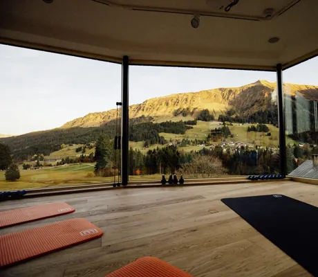 Aussicht vom Fitnessraum des Hotel Sonnenburg auf Bergpanorama mit bodenlangen Glasfronten und Sportmatten.