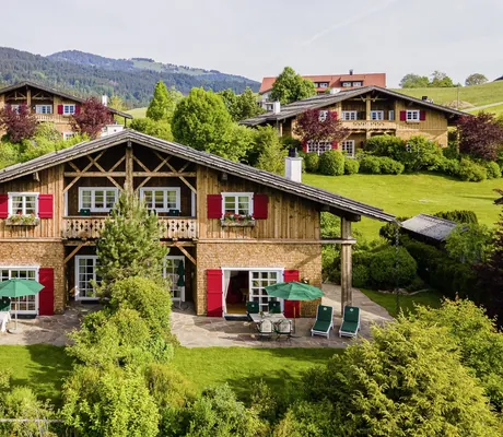 Außenansicht eines charmanten Alpenchalets im Sonnenalp Resort mit roten Fensterläden, Terrasse und umgeben von grüner Landschaft
