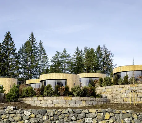 Außenansicht der NaturLodges des Sonnenalp Resorts mit runden Holzfassaden, Steinmauern, Pflanzen und Bäumen im Hintergrund