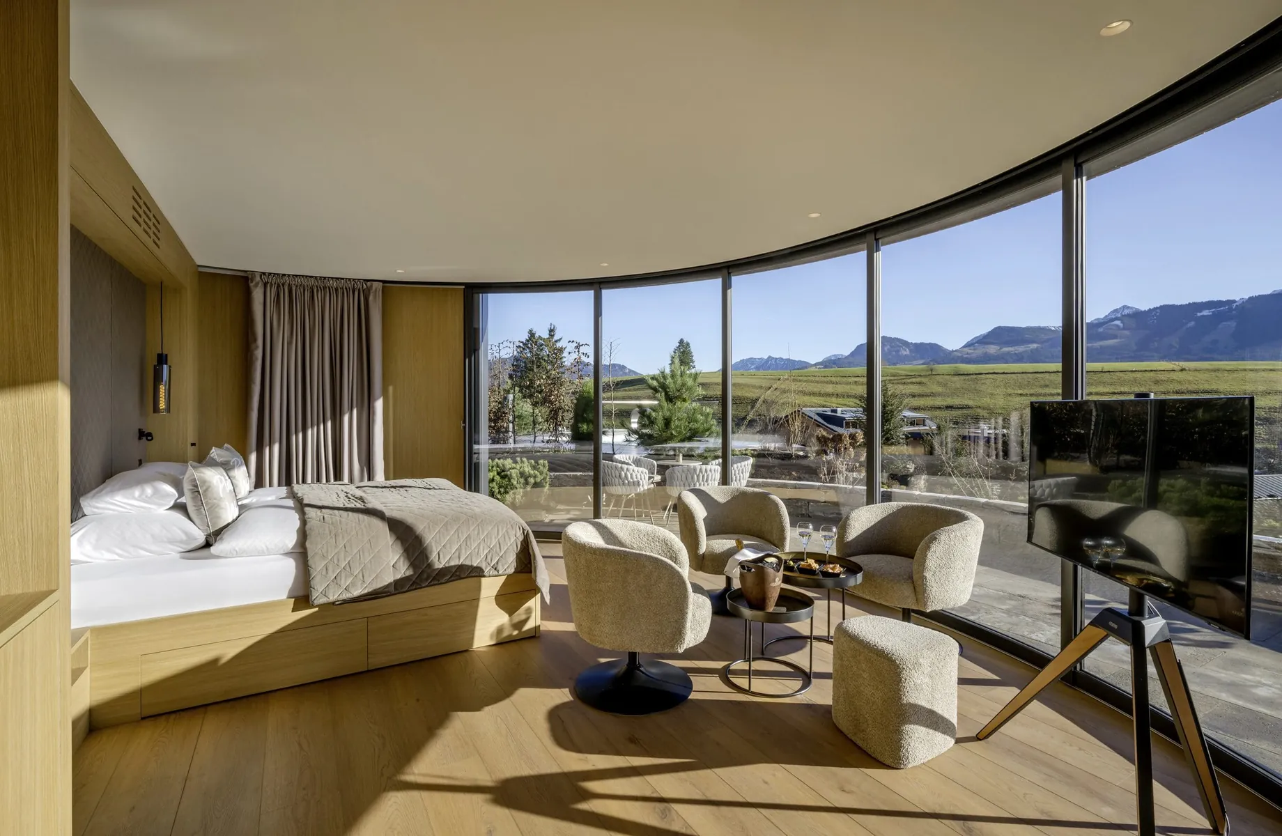 Innenansicht einer NaturLodge des Sonnenalp Resorts mit Doppelbett, Sitzbereich und Panorama-Fensterfront mit Blick auf Terrasse und Berge