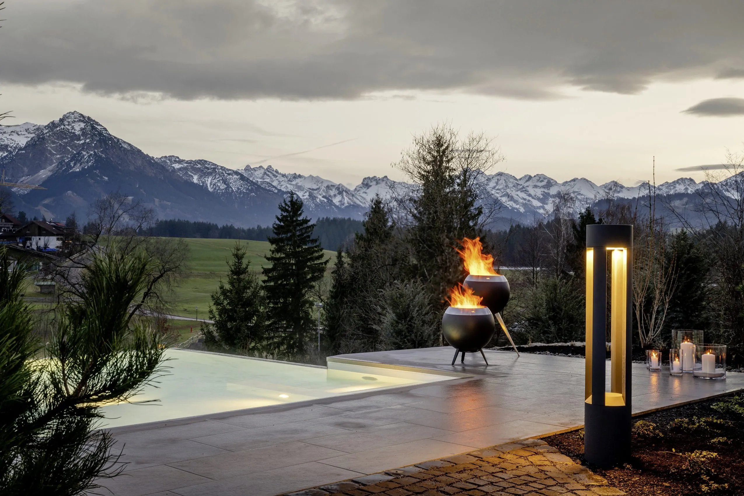 Außenpool einer NaturLodge des Sonnenalp Resorts mit Feuerstellen, Kerzen und Bergblick bei Dämmerung