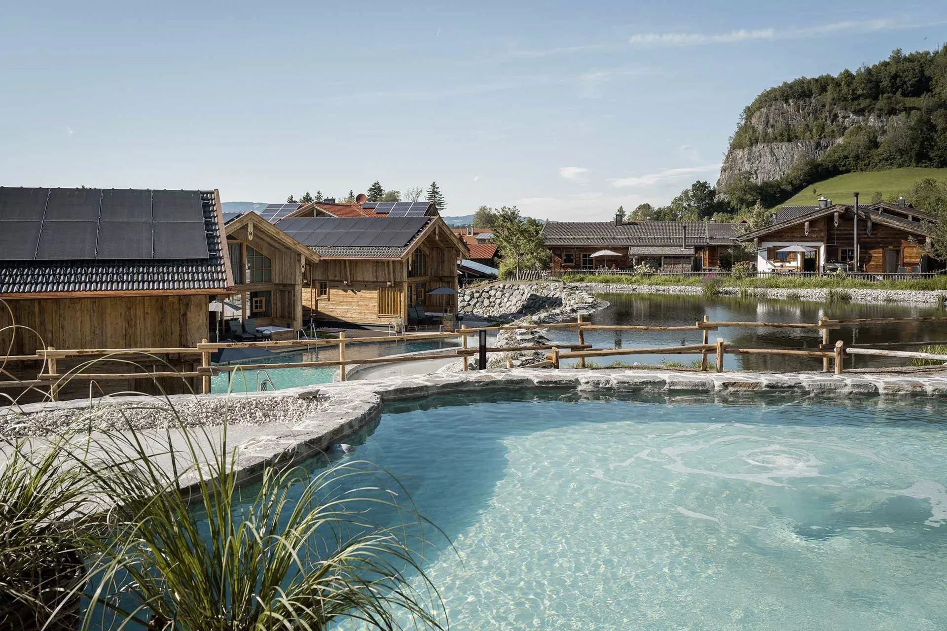 Blick auf die Anlage der Alpzitt-Chalets in Bayern mit Naturbadesee und Berglandschaft im Hintergrund