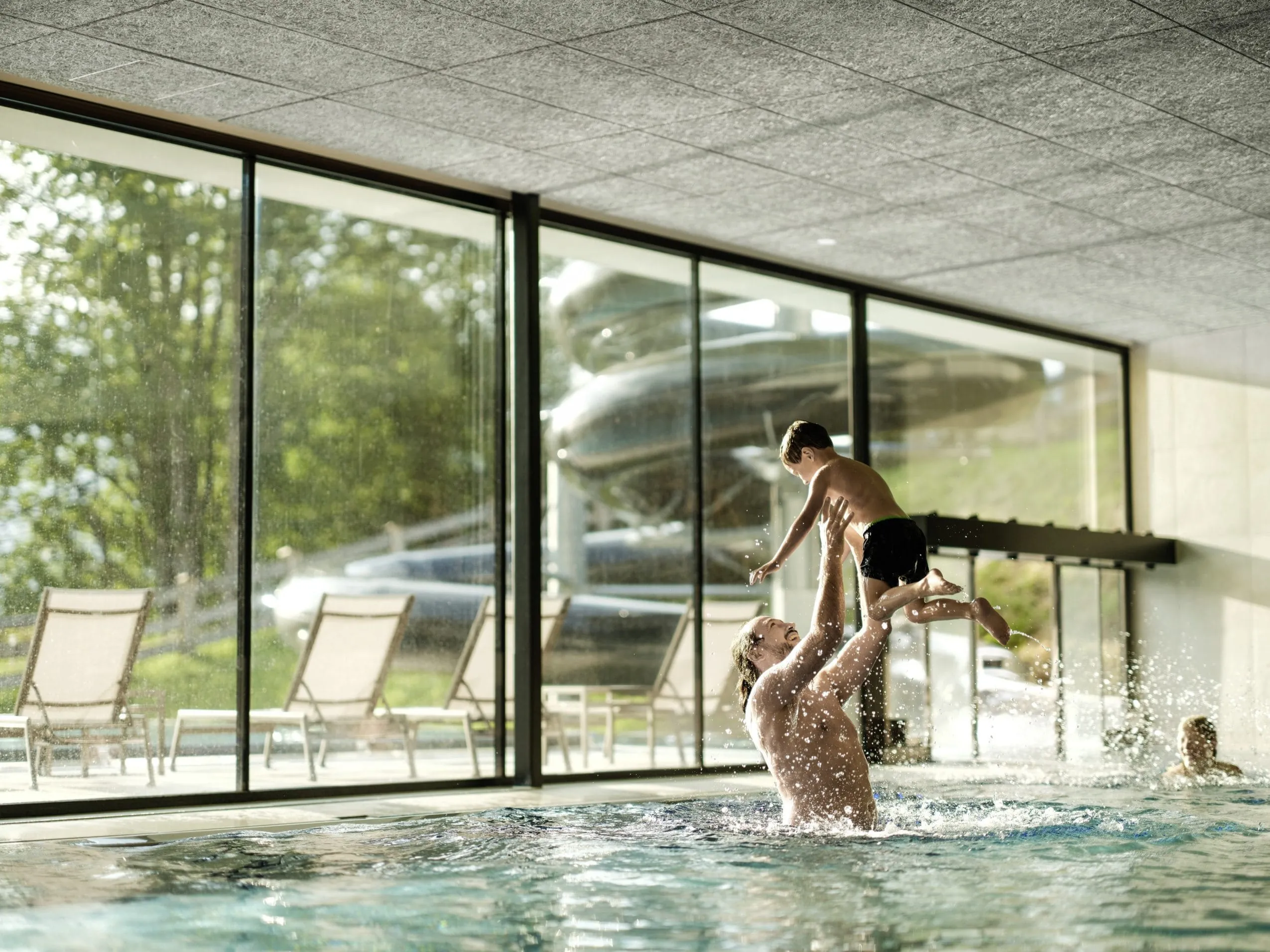 Vater spielt mit Kind im Indoorpool des Falkensteiner Family Hotels Montafon, große Fenster mit Blick nach draußen