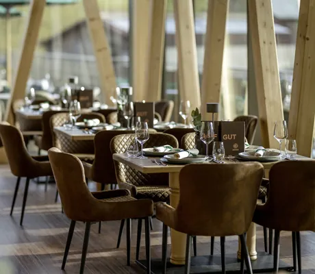 Gedeckte Tische mit braunen Polsterstühlen im Hofgut-Restaurant des Sonnenalp Resorts, mit großen Holzsäulen und Blick nach draußen