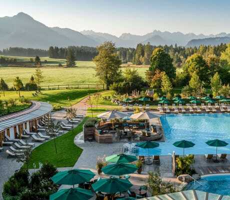 Blick von oben auf die Outdoorpool-Landschaft des Sonnenalp Resorts, im Hintergrund die Allgäuer Berge