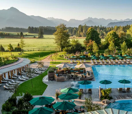 Blick von oben auf die Outdoorpool-Landschaft des Sonnenalp Resorts, im Hintergrund die Allgäuer Berge