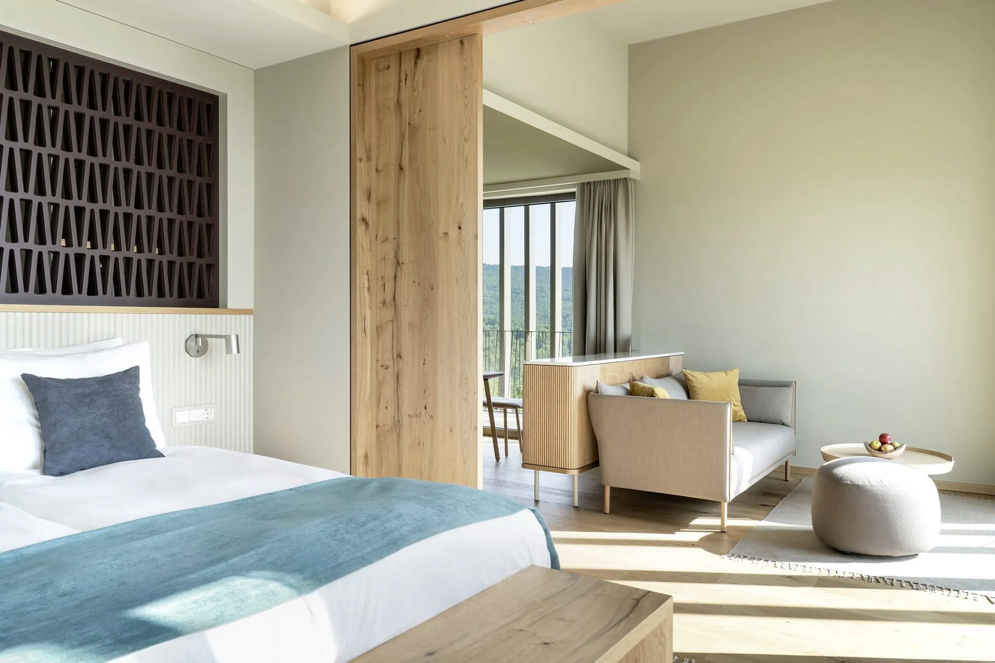 Zimmer im WALD.WEIT Rheingau Hotel & Retreat mit türkisem Bettüberwurf und Sitzecke mit grauem Sofa