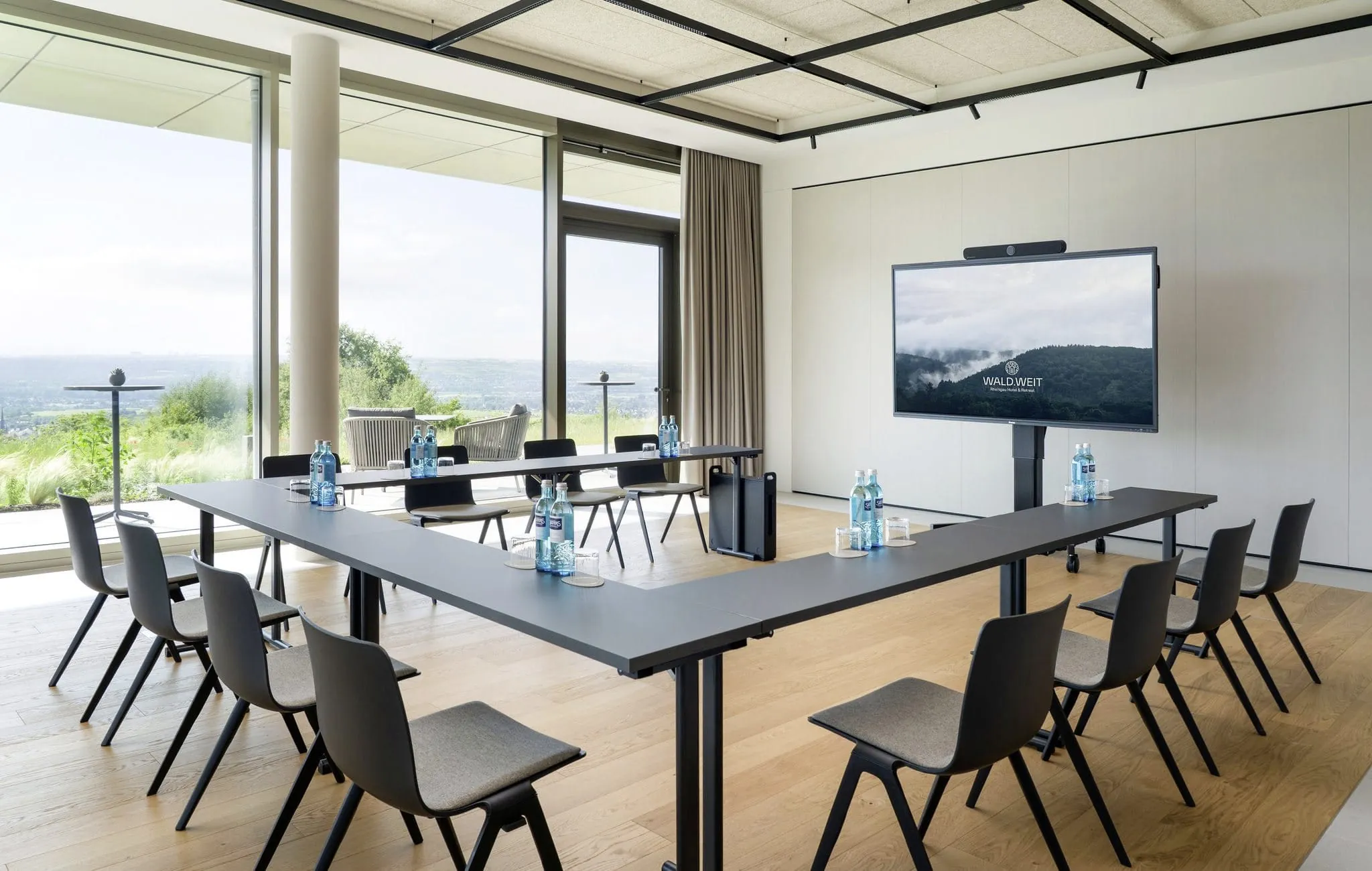 In U-Form bestuhlter Tagungsraum im WALD.WEIT Rheingau Hotel & Retreat mit Monitor und großem Panoramafenster