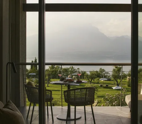 Blick vom Zimmer des Cape of Senses auf den Balkon mit zwei Rattanstühlen und den Gardasee
