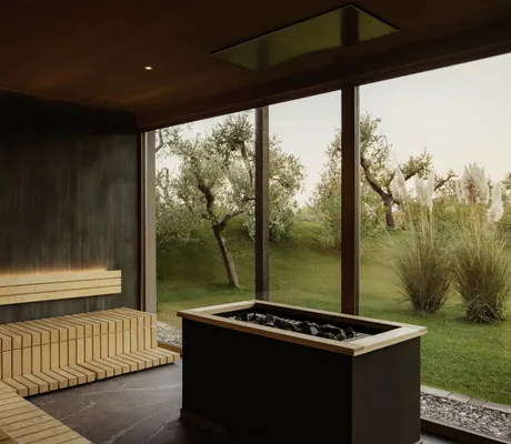 Sauna im Cape of Senses mit großem Saunaofen und Blick auf den Garten mit Bäumen und Gräsern