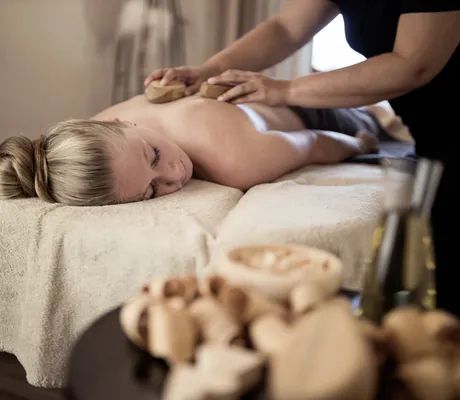 Zirbenholzraspel und Ölflasche neben Massageliege mit blonder Frau im DAS GERSTL Alpine Retreat