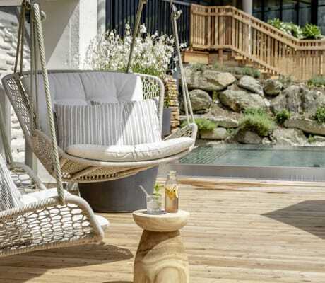 Zwei Hängesessel mit Kissen auf einer Holzterrasse, im Hintergrund Pflanzen und ein Pool im DAS.GOLDBERG