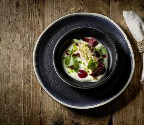 Gourmetgericht auf dunklem Keramikteller, angerichtet auf rustikalem Holztisch mit Stoffserviette im DAS.GOLDBERG