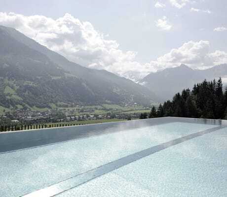Outdoorpool des DAS.GOLDBERG mit Blick auf grüne Täler und Berge unter bewölktem Himmel