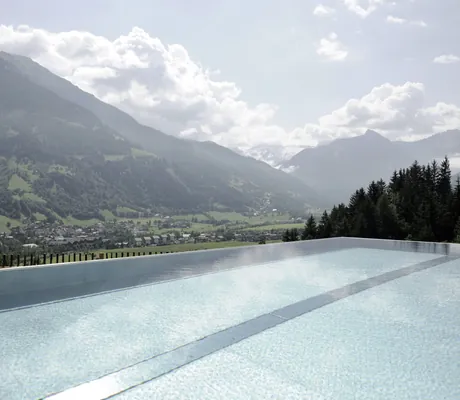 Outdoorpool des DAS.GOLDBERG mit Blick auf grüne Täler und Berge unter bewölktem Himmel