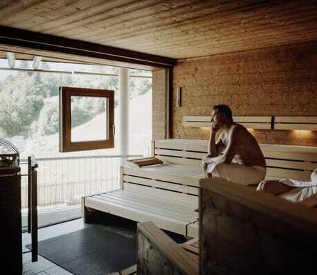 Paar in weiße Handtücher gewickelt schaut aus dem Fenster der Sauna im DAS.GOLDBERG