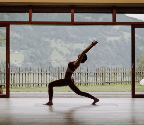 Frau beim Yoga in einer Pose vor großen Fenstern mit Bergblick und Holzboden im DAS.GOLDBERG