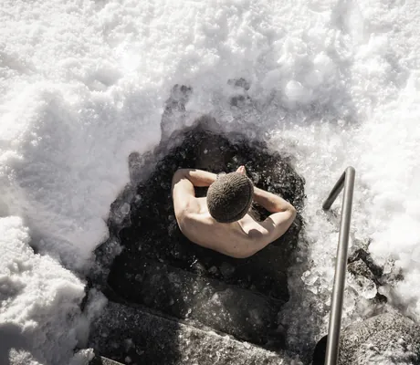 Mann mit Mütze sitzt im Eisbad im Natursee des Wellnesshotel Der Engel