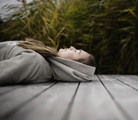 Frau mit Bademantel liegt auf Holzsteg am Natursee des Wellnesshotel Der Engel