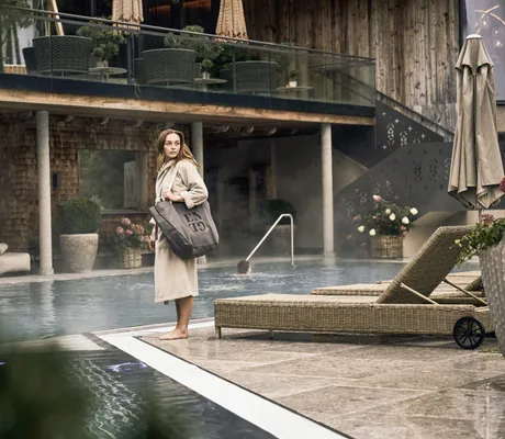 Frau im Bademantel steht im Wellnesshotel Der Engel mit Badetasche am Außenpool