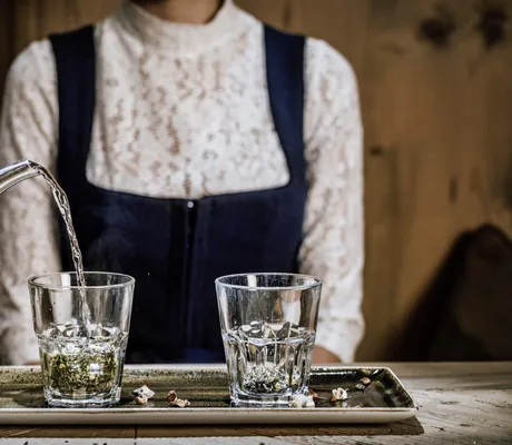im Wellnesshotel Der Engel wird einer Frau im Dirndl am Tisch Tee eingeschenkt
