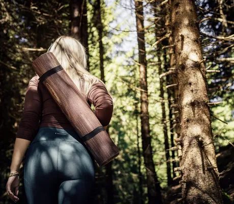 blonde Frau geht im Wellnesshotel Der Engel mit Yogamatte in den Wald